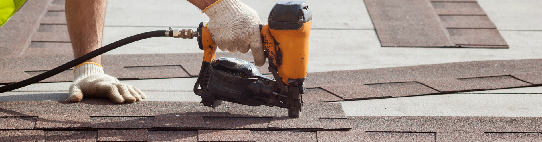 Close up shot of a worker with gloves installing new shingles on a residential roof with a nail gun